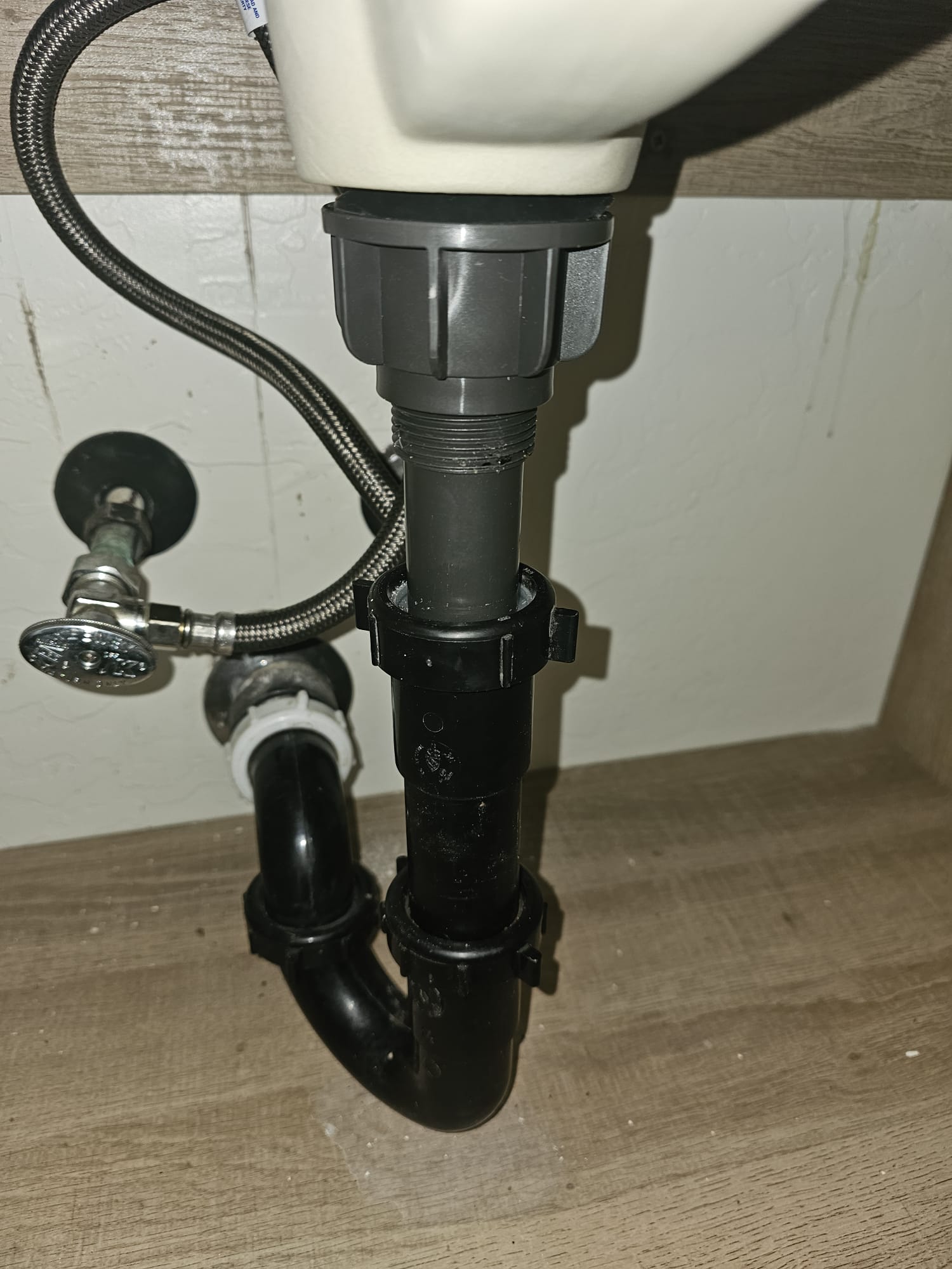 Under-sink plumbing setup with pipes and fixtures on a wooden floor.